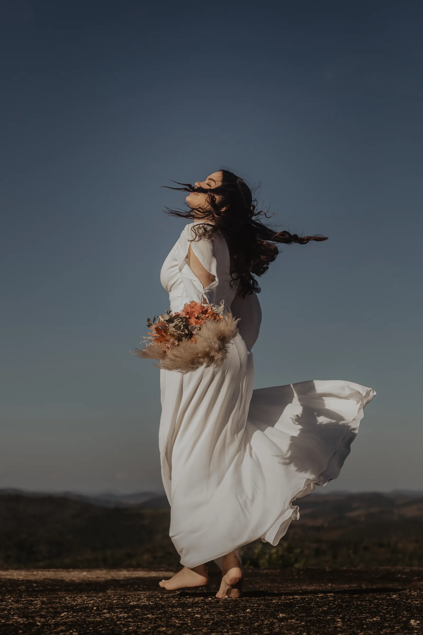 Retrato com o vestido em movimento ao vento, sob céu aberto.